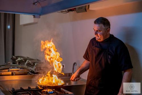 a man cooking food in a frying pan with flames at May Beach Hotel in Rethymno Town