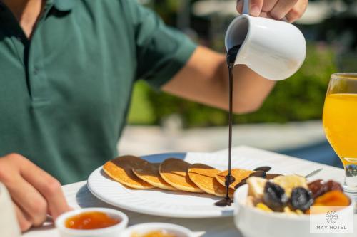 a person pouring syrup onto a plate of food at May Beach Hotel in Rethymno Town