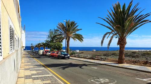 a street with palm trees and cars parked on the side of a beach at "Burrero Bay Høme" Geniu's Best Selection - Airport Homely Stays in Playa del Burrero