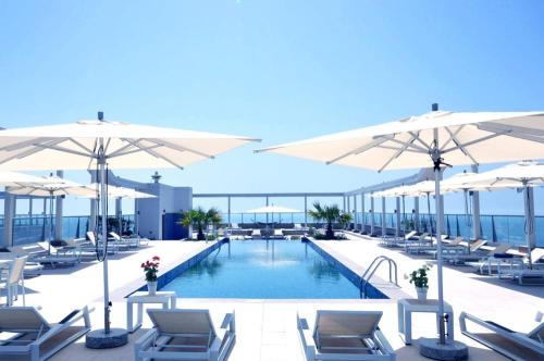 a pool with chairs and umbrellas on a building at 2 Bedroom Deluxe Beach Apartment Al Marjan in Ras al Khaimah