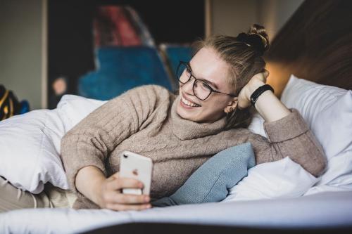 a woman sitting on a bed holding a cell phone at Hotel Atlantic in Aarhus