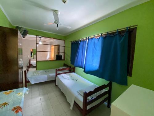 2 camas en una habitación con paredes verdes y cortinas azules en Hotel Mar Casado, en Guarujá