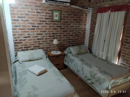 1 dormitorio con 2 camas y pared de ladrillo en Cabañas Rincón del Río en Colón