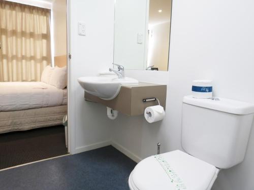 a bathroom with a toilet and a sink and a bed at Tetra Serviced Apartments by Nesuto in Auckland