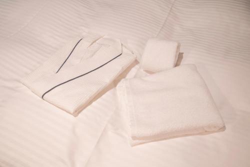 duas toalhas brancas em cima de uma cama em Hotel R9 Sano Fujioka em Sano
