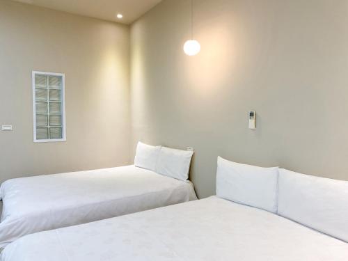 two beds in a room with white sheets and a window at 羅東微風小棧民宿 in Luodong
