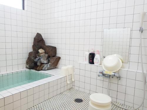a white tiled bathroom with a tub and a toilet at Pilot Lodge in Hakuba