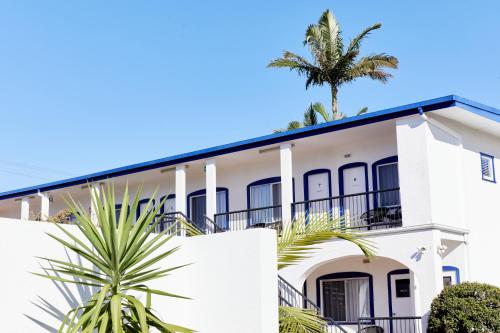 a white house with a palm tree in the background at The Sails Motel Brunswick Heads in Brunswick Heads