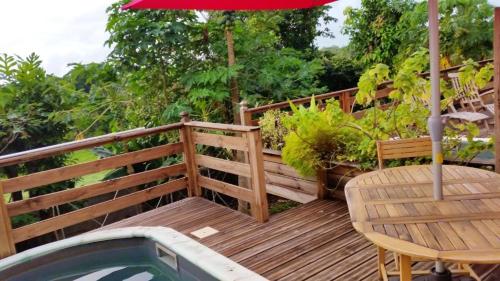 una terraza de madera con mesa y sombrilla en Maison d'une chambre avec vue sur la mer piscine privee et jacuzzi a Le Moule, en Le Moule