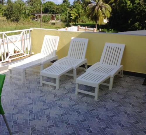tres sillas blancas sentadas junto a una pared amarilla en Appartement de 2 chambres avec jardin clos et wifi a Le Moule a 3 km de la plage, en Le Moule