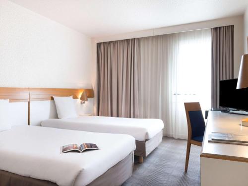 a hotel room with two beds and a television at Novotel Paris Est in Bagnolet