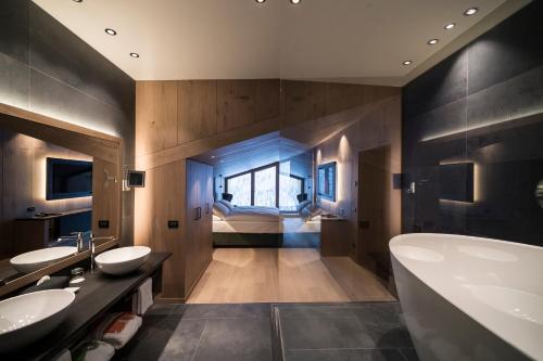 a bathroom with two sinks and a tub and a bedroom at Hotel Cappella in Colfosco