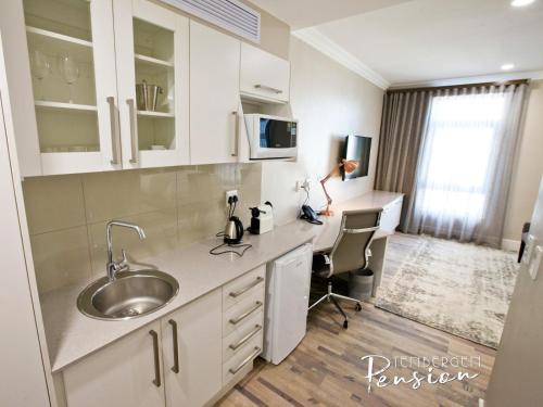 a kitchen with white cabinets and a sink and a desk at Tenbergen Pension Hotel in Windhoek