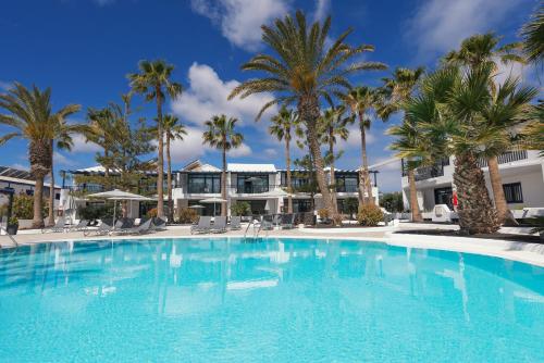 uma grande piscina com palmeiras em frente a um edifício em Apartamentos Playamar em Puerto del Carmen