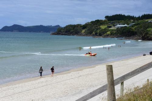 a group of people on a beach with a boat in the water at Camp Waipu Cove in Waipu