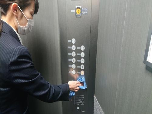 Une femme dans un masque appuie sur un bouton sur un ascenseur dans l'établissement Smile Hotel Hakataekimae, à Fukuoka