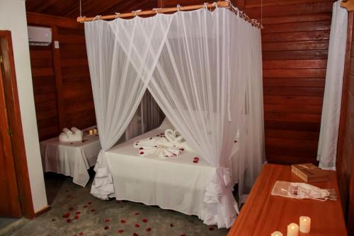 a room with a bed with white curtains and a table at Pousada Bahia-Nova Caraíva in Caraíva