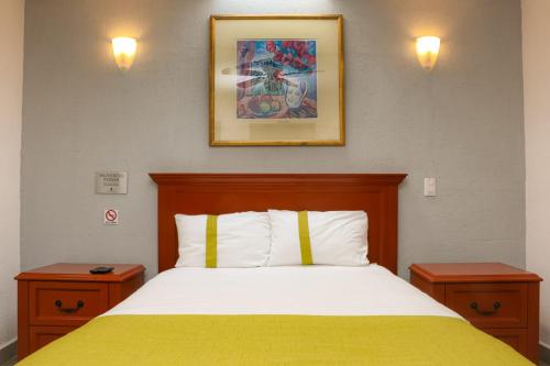 a bedroom with a bed with a yellow blanket and two tables at Suites Bajío in León