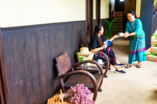 two women are sitting in a room with a woman holding a cup at Ban Kong Rao Guesthouse in Chiang Mai