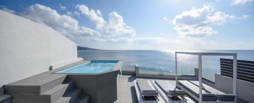 a balcony with a swimming pool and chairs and the ocean at Sublime Villa & Caves in Akrotiri