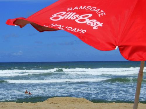 a red umbrella on the beach with people in the ocean at Crayfish Inn no5 in Ramsgate