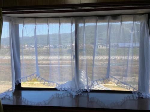 a window with white curtains and a view of a field at 古民家ゲストハウス穏 in Sakaide