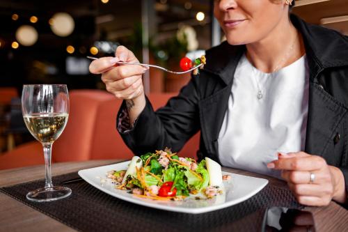 a woman eating a plate of food with a glass of wine at Novotel Criciuma in Criciúma