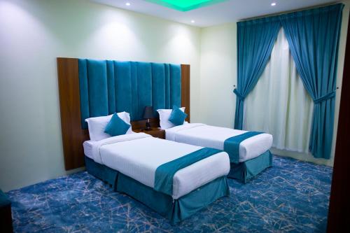two beds in a hotel room with blue curtains at فندق بــــاســــيل in Hafr Al Baten