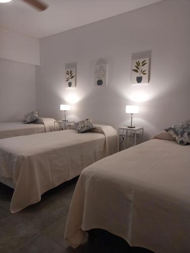 two beds in a white room with two lamps at Complejo Pirovano in Lincoln