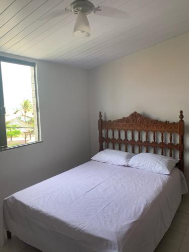 a bedroom with a bed with white sheets and a window at CASA NA PRAÇA DE AREMBEPE in Arembepe