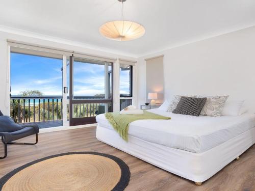 a white bedroom with a large bed and a balcony at Panorama Place on Jones Beach in Minnamurra