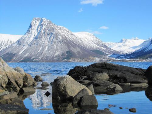 a snow covered mountain in front of a body of water at Skomakergarden in Ulsteinvik