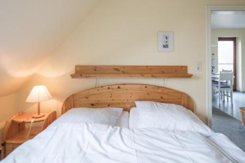 BorgsumにあるFerienwohnung in Borgsum (oben rechts)の白いベッド1台(木製ヘッドボード付)が備わるベッドルーム1室が備わります。