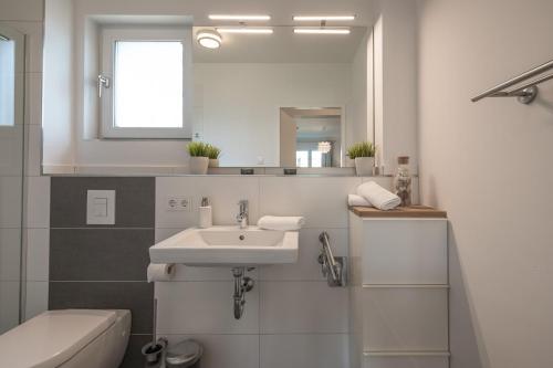 ein weißes Badezimmer mit einem Waschbecken und einem Spiegel in der Unterkunft Hafenquartier 54° in Husum