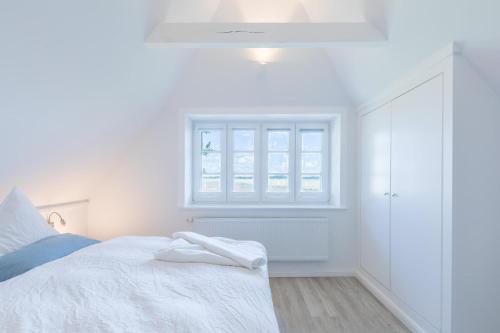 a white bedroom with a bed and a window at Reethus Backbord Dagebüll in Dagebüll