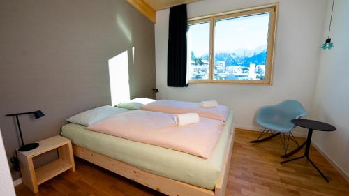 a bedroom with a bed and a window and a chair at Laax wellnessHostel3000 in Laax