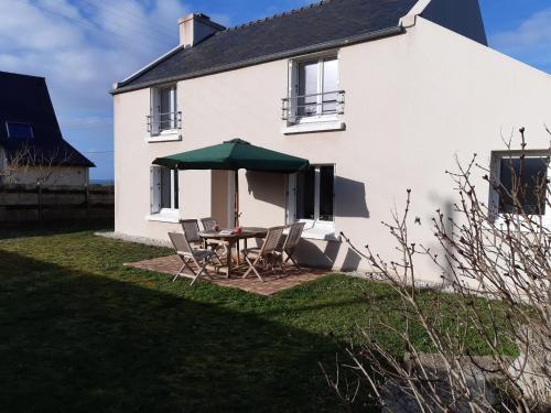 a white house with a table and a green umbrella at Les embruns in Plouarzel