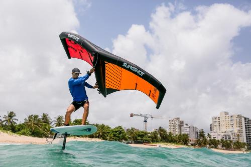 mężczyzna stoi na desce surfingowej na wodzie w obiekcie Numero Uno Beach Apartments w mieście San Juan