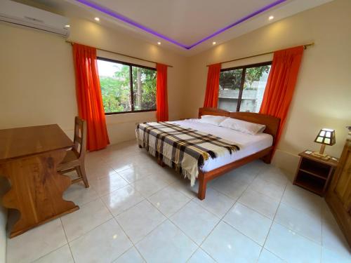 a bedroom with a bed and a desk and two windows at Hostal Vista al Mar in Puerto Ayora