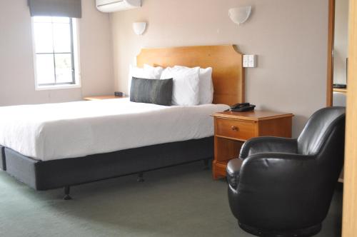 a hotel room with a bed and a leather chair at City Suites in Tauranga