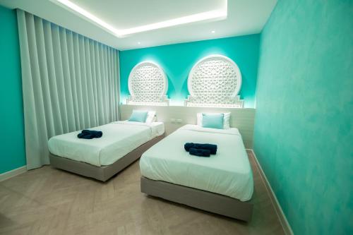 two beds in a room with blue walls and windows at Le Maroc Hotel Patong in Patong Beach