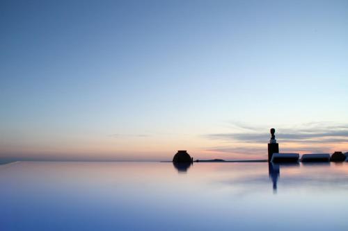 a silhouette of a lighthouse on the water at sunset at The Tsitouras Collection in Firostefani