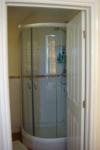 a shower with a glass door in a bathroom at Harlequin Guest House with parking in Weymouth