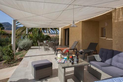 un patio con sofá, sillas y sombrilla en Appartement de vacances Arbousier à Calvi piscine chauffée partagée bbq en Calvi
