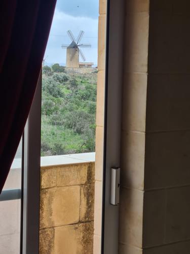 a window with a view of a windmill from a building at Il Bejta penthouse in Qala