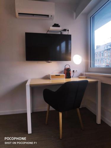 a desk with a chair and a television on a wall at DayNight Sauveniere in Liège