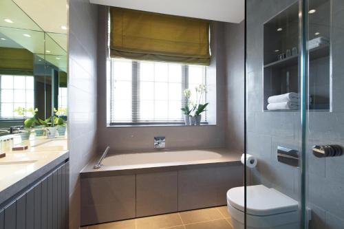 a bathroom with a tub and a toilet and a window at AKA Marylebone in London