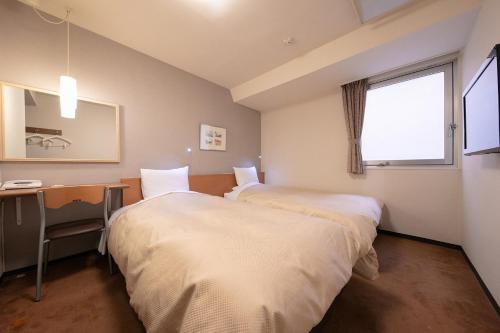 two beds in a room with a desk and a window at Morioka City Hotel in Morioka