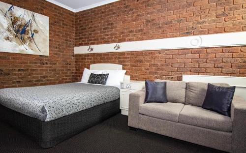 a bedroom with a bed and a couch next to a brick wall at Albury Townhouse Motel in Albury