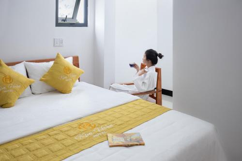 a woman sitting in a chair next to a bed at Kim Hoàn Hotel Phan Rang in Phan Rang